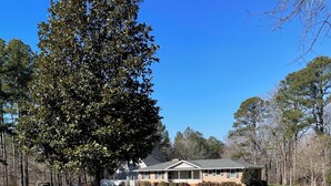 A house with a large lawn, a gravel driveway, and a tree in the foreground. - Masters 2027 Secluded Charming House in the Pines (Harlem)