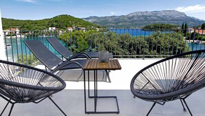 A balcony with two lounge chairs, a small table, and a view of a lake and mountains. - Beachfront Orange Apartment (Žrnovo)