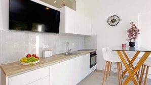 A modern kitchen with white cabinets, a wooden countertop, a sink, and a dining area with a table and chairs. - Beachfront Orange Apartment (Žrnovo)