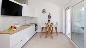 A modern kitchen with white cabinetry, a wooden countertop, and a dining area with a glass table and white chairs. - Beachfront Orange Apartment (Žrnovo)