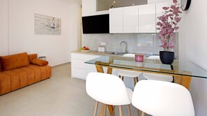 A modern kitchen with a glass dining table, white chairs, a sofa, and a potted plant. - Beachfront Orange Apartment (Žrnovo)