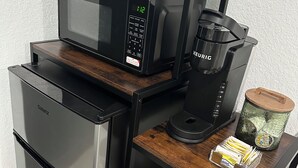 Kompakti keittokomero, jossa on Galanz-merkkinen jääkaappi, Keurig-kahvinkeitin, mikroaaltouuni sekä pieni kahvinurkkaus, jossa on kuppeja ja pulloja.