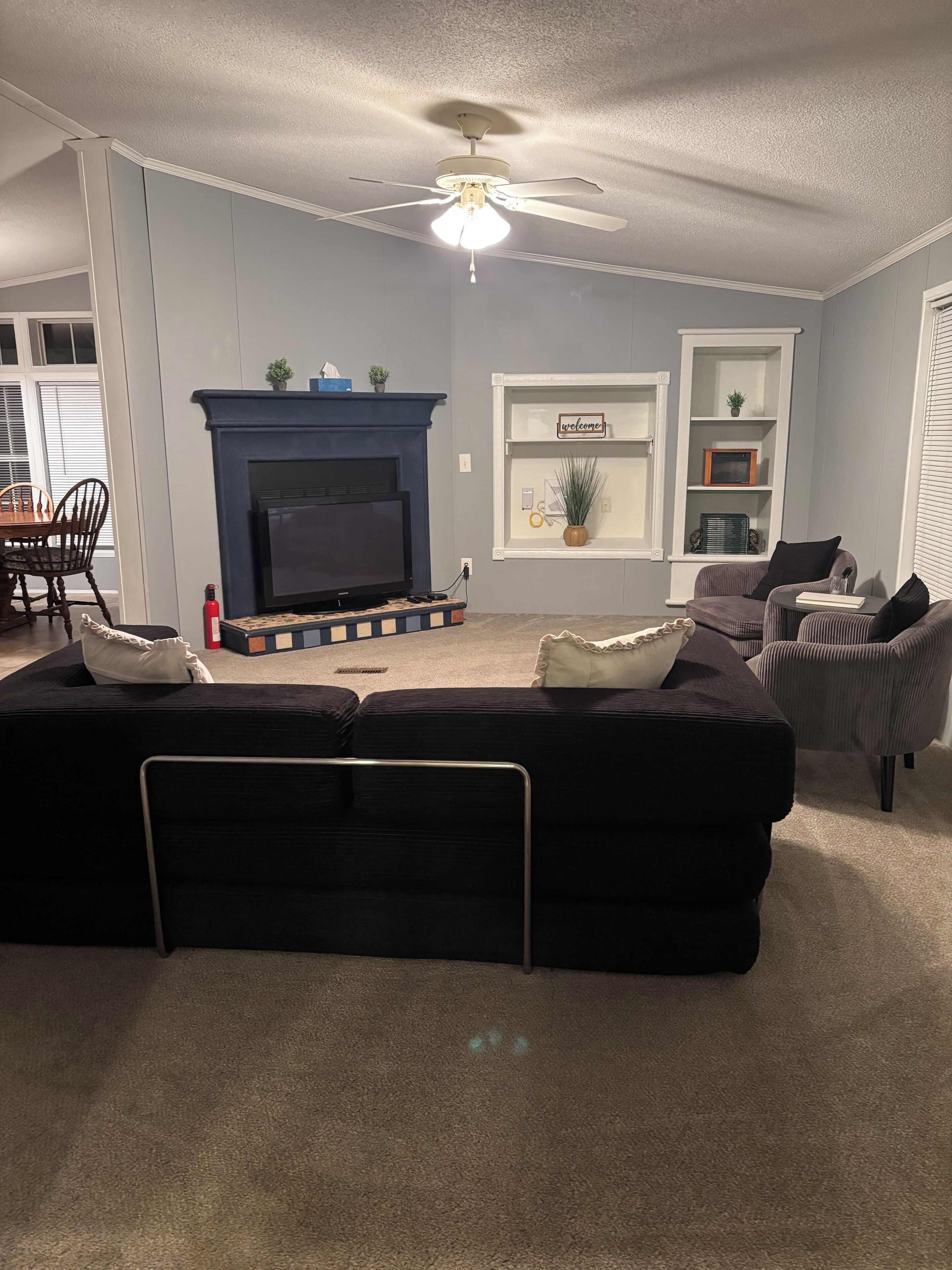 A living room with a black sectional sofa, a fireplace, a television, and a ceiling fan.