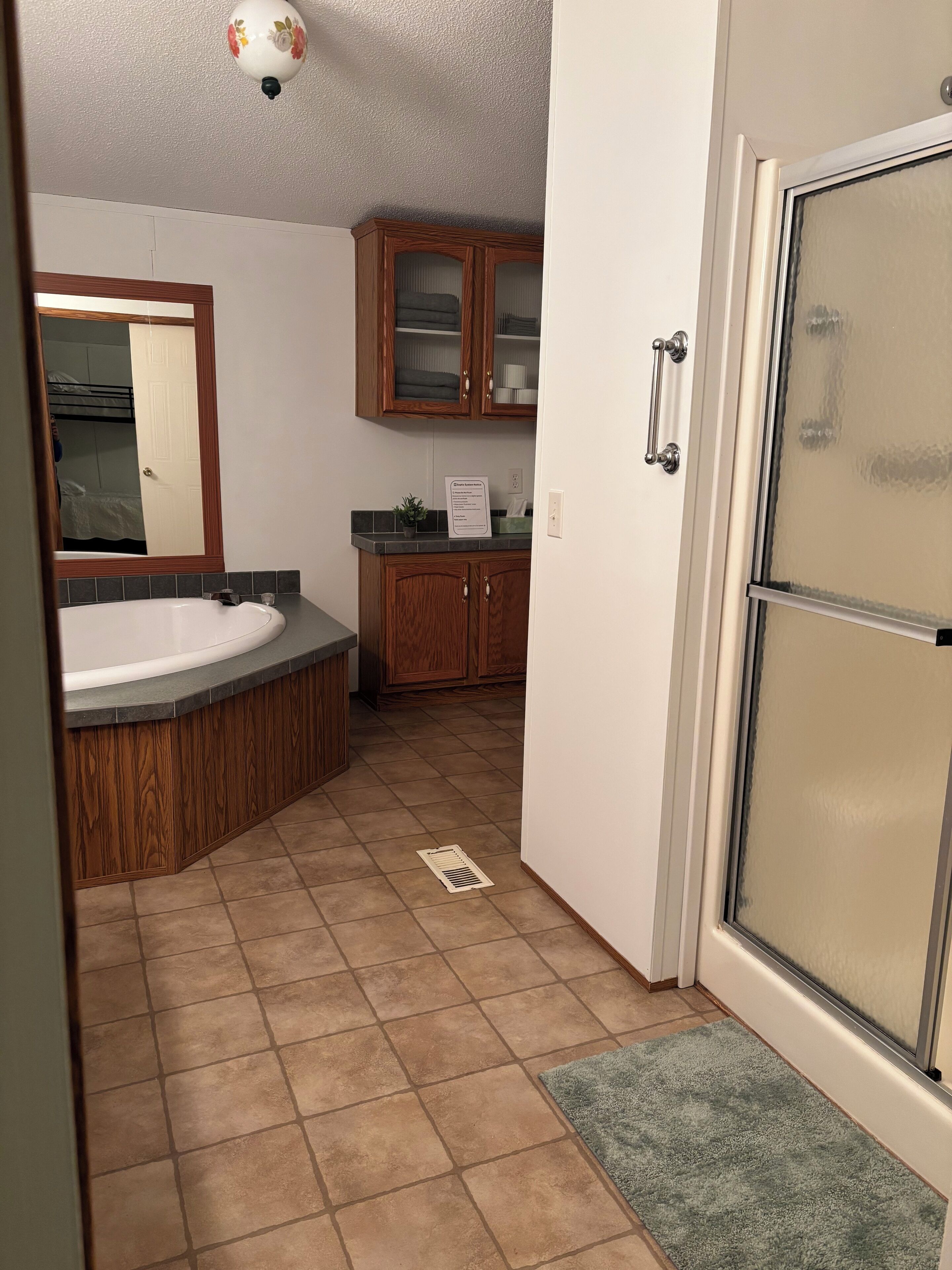 A bathroom with a bathtub, wooden cabinets, a mirror, and a shower area.