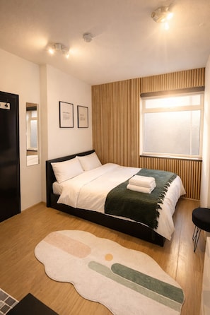 Ein Schlafzimmer mit Bett, Fenster, Holzvertäfelung und einem kleinen Teppich.