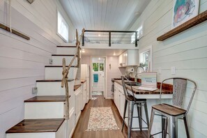 A compact kitchen with a dining area, wooden steps, and a loft bedroom with a bunk bed. - Tiny House Paradise - Pool, Spa, Slide, Beaches (Bradenton)