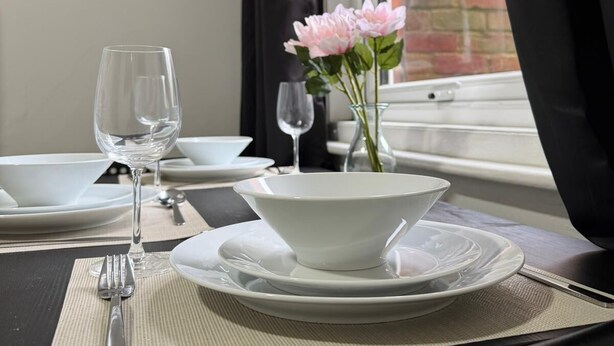 A dining table set with white plates, bowls, a wine glass, and a vase with pink flowers. - Amazing Garden Apartment - Miami Lodge (Reading)
