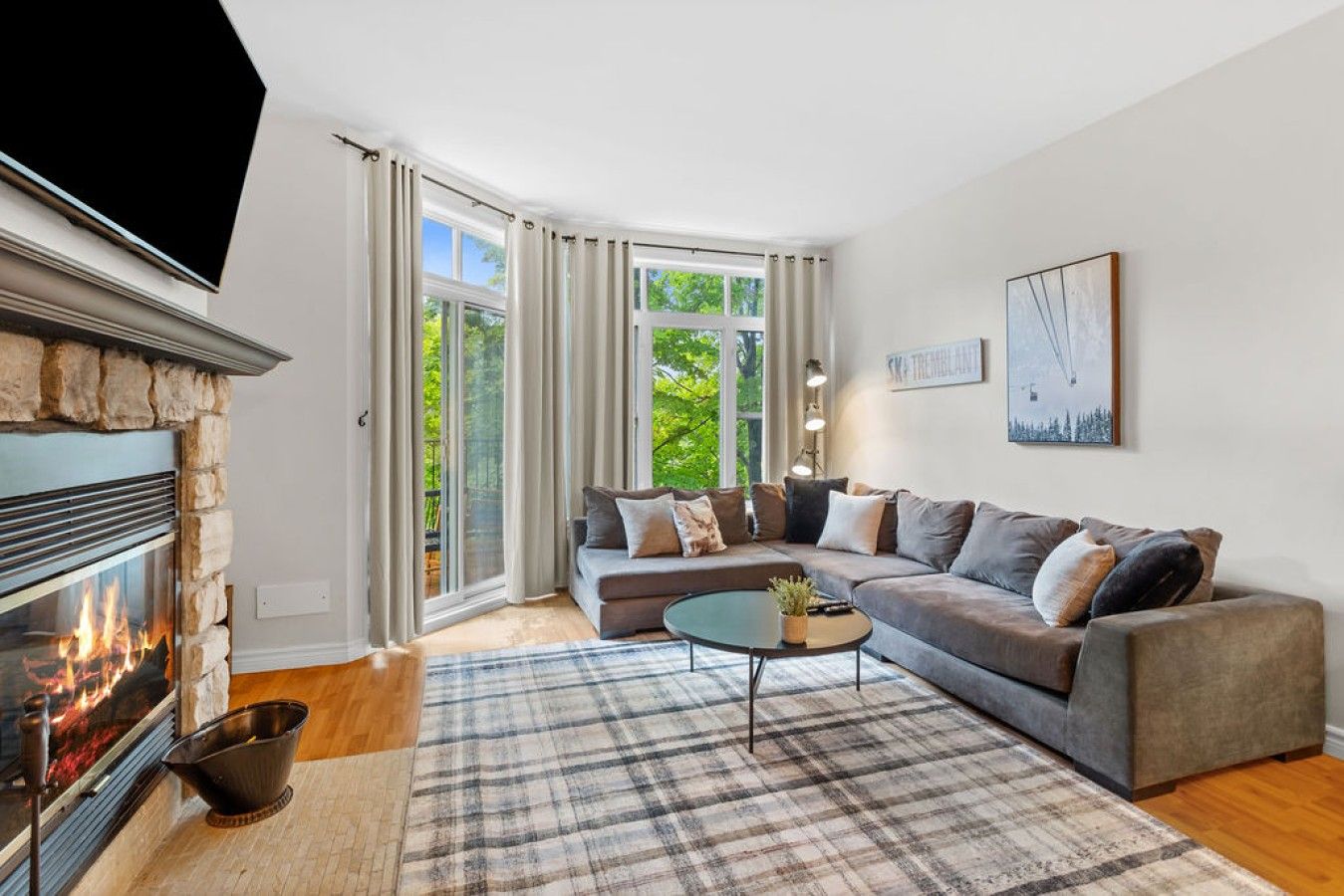 A modern living room with a fireplace, a sectional sofa, a coffee table, and a large window with curtains.