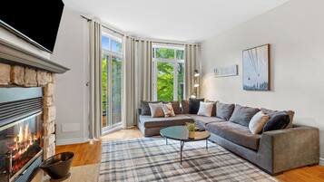 A modern living room with a fireplace, a sectional sofa, a coffee table, and a large window with curtains.