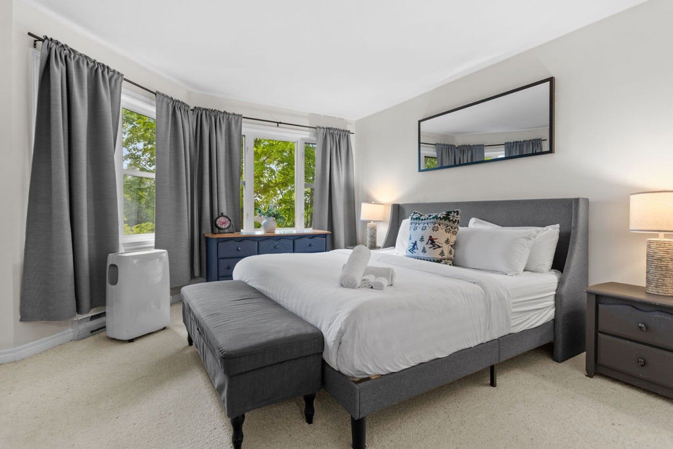 A bedroom with a bed, a bedside table, a nightstand, a dresser, and a window with curtains.