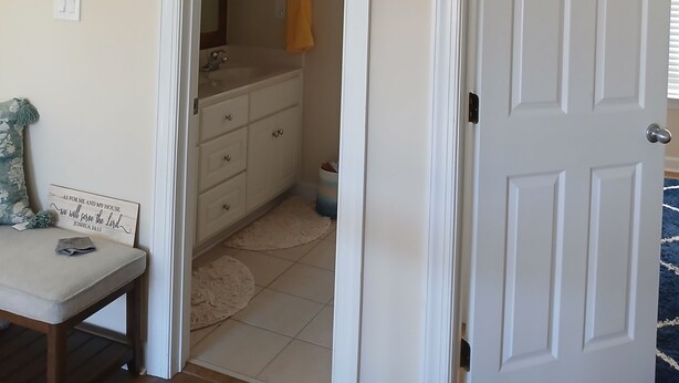 Une pièce avec une porte blanche, un miroir, un lavabo et un porte-serviettes.
