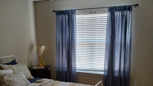Une chambre à coucher avec un lit, une table de chevet, un ventilateur de plafond et une fenêtre avec des rideaux.