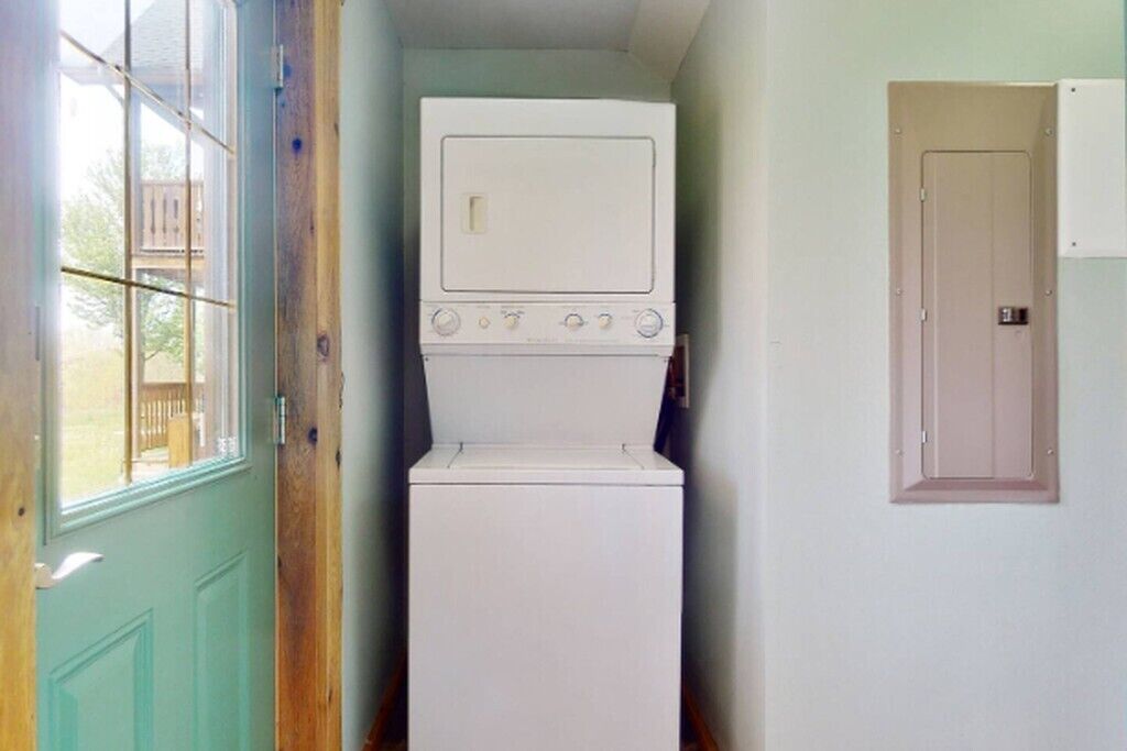 A laundry room with a washer and dryer stacked against a wall, a wooden door, and a window.