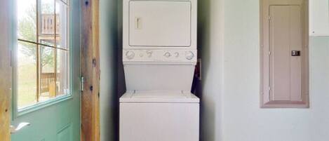 A laundry room with a washer and dryer stacked against a wall, a wooden door, and a window.