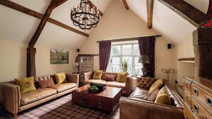Een knus loft-woonkamer met zichtbare houten balken, een kroonluchter en een vloer met ruitmotief.
