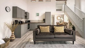 Un espace de vie moderne comprenant un canapé gris, des meubles de cuisine, un escalier et un coin repas.