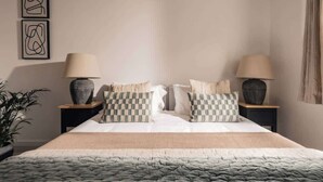 Une chambre à coucher bien aménagée, avec un grand lit, deux tables de chevet dotées de lampes et des œuvres d’art abstraites accrochées au mur.