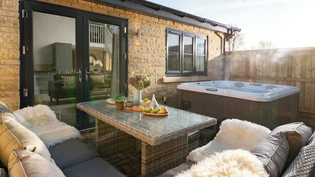 Un espace patio avec une porte vitrée donnant sur une pièce, un jacuzzi, des meubles en osier et une table garnie de fruits.