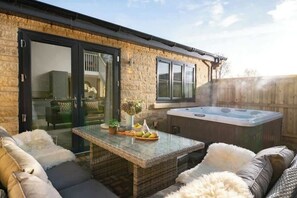 Un espace patio avec une porte vitrée donnant sur une pièce, un jacuzzi, des meubles en osier et une table garnie de fruits.