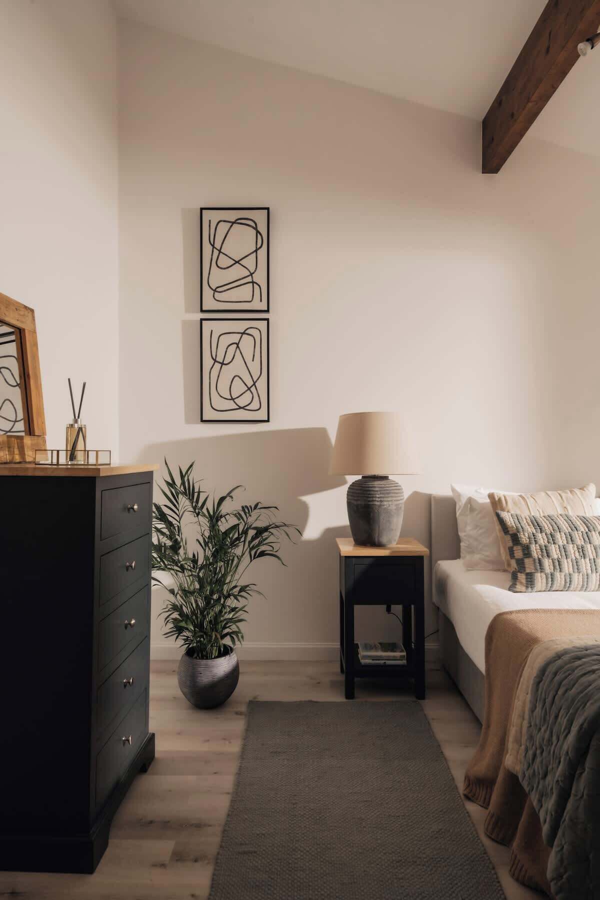A bedroom with a bed, a dresser, a nightstand, a lamp, and two abstract paintings on the wall.