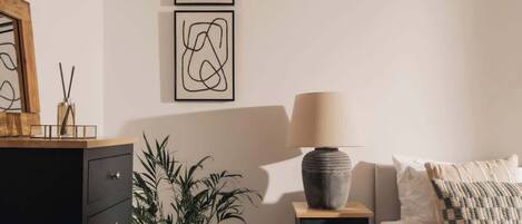 A bedroom with a bed, a dresser, a nightstand, a lamp, and two abstract paintings on the wall.