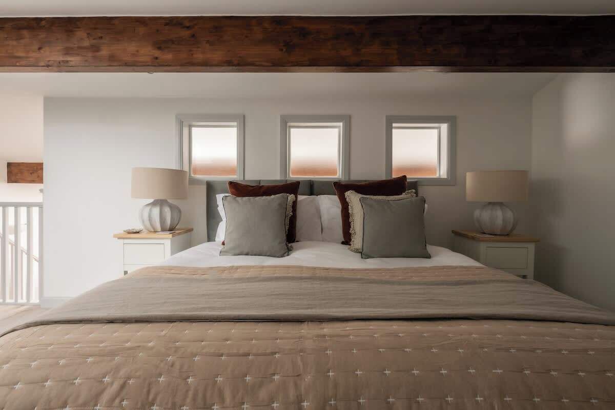 A bedroom with a large bed, three bedside lamps, and a view through three windows.