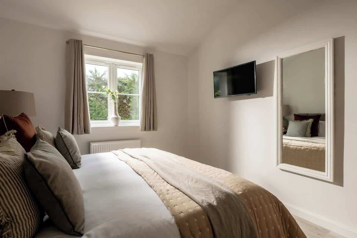 Ein Schlafzimmer mit Bett, Wandfernseher, Fenster mit Vorhängen und Spiegel.