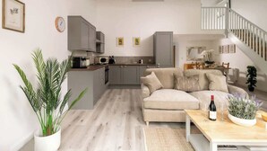 Una sala moderna con un sofá beige, una mesa de centro de madera y una cocina al fondo.