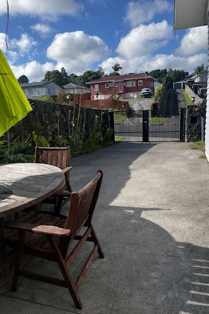 Un patio con una mesa y sillas de madera redonda, un portón de metal negro y un edificio rojo al fondo.