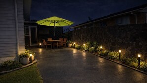 Eine gepflasterte Terrasse mit Tisch, Stühlen, Sonnenschirm und dekorativer Beleuchtung.