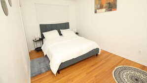 A bedroom with a bed, a nightstand, a window with blinds, a wall-mounted painting, and a patterned rug. - Cozy 3 bedroom home close to all amenities (Winnipeg)