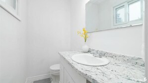 A bathroom with a white sink, a marble countertop, a white toilet, and a vase with yellow flowers on the counter. - Cozy 3 bedroom home close to all amenities (Winnipeg)