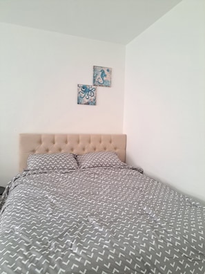 Ein Schlafzimmer mit einer geblümten Kopfteil, einer gemusterten Bettdecke und zwei an der Wand befestigten Kunstwerken.