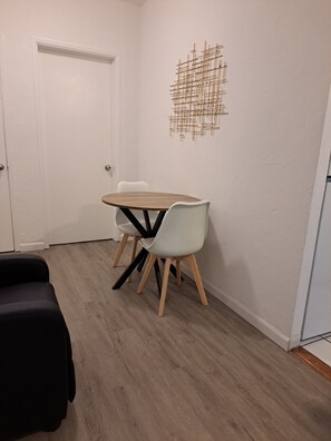 Ein kleiner Essbereich mit einem runden Tisch, zwei Stühlen, einer weißen Tür und einem an der Wand hängenden abstrakten Kunstwerk.