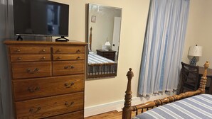 A bedroom with a wooden dresser, a bed with a striped pillow, a mirror, and a television on a stand.