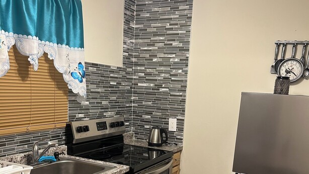 A modern kitchen with a stainless steel refrigerator, an oven, a sink, and a stove.