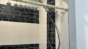 A shower with a black and white tiled wall, a chrome showerhead, and a handheld showerhead.