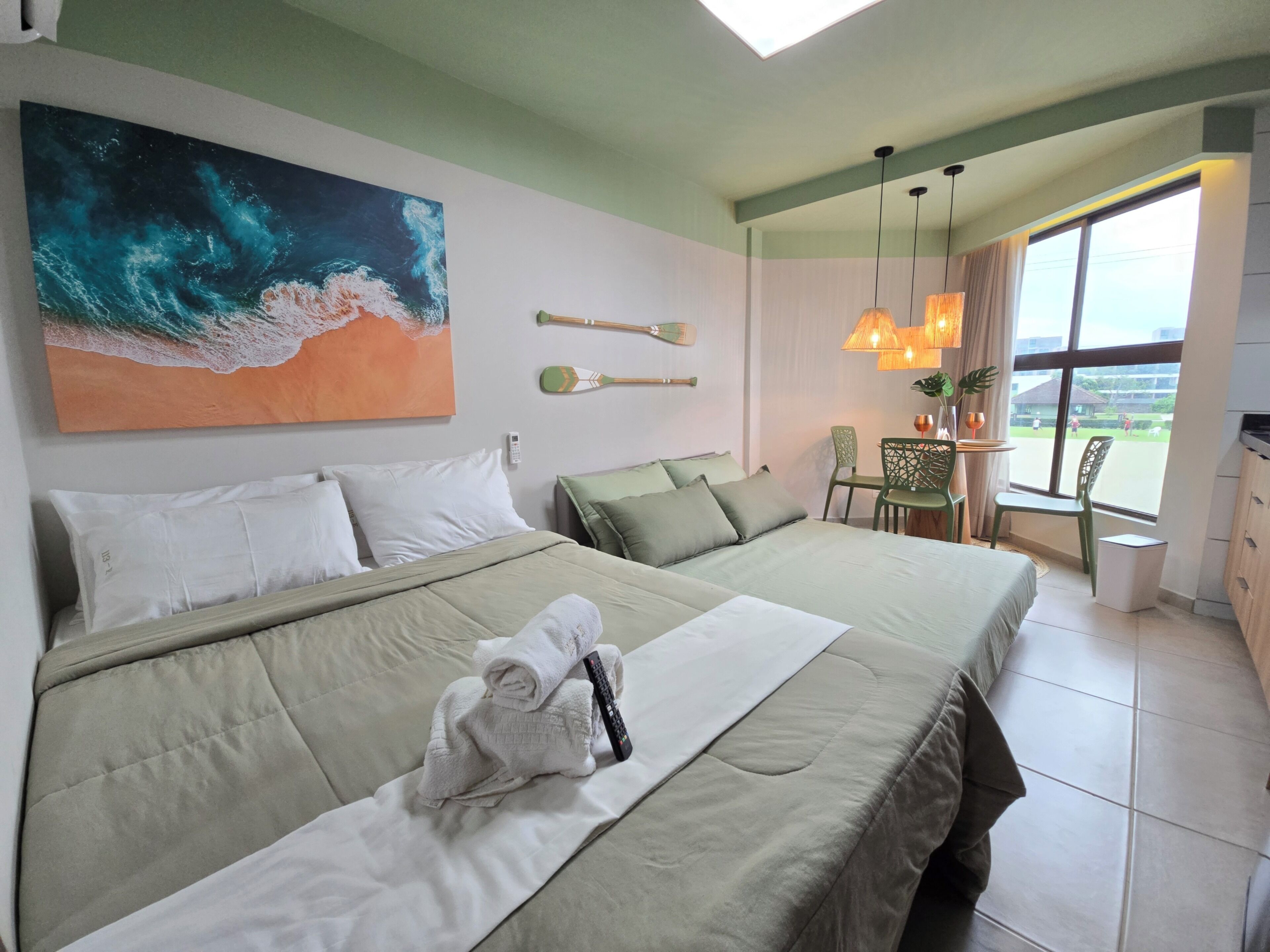 A hotel room with a bed, a painting, a desk with a chair, and a view through the window.