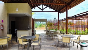 An outdoor patio area with a covered seating arrangement, a grill, and a view of the surrounding landscape. - Studio 5.0 ★ | Condo with Pool + Hot Tub | 5 min from Brazil's most famous beach (Tamandaré)