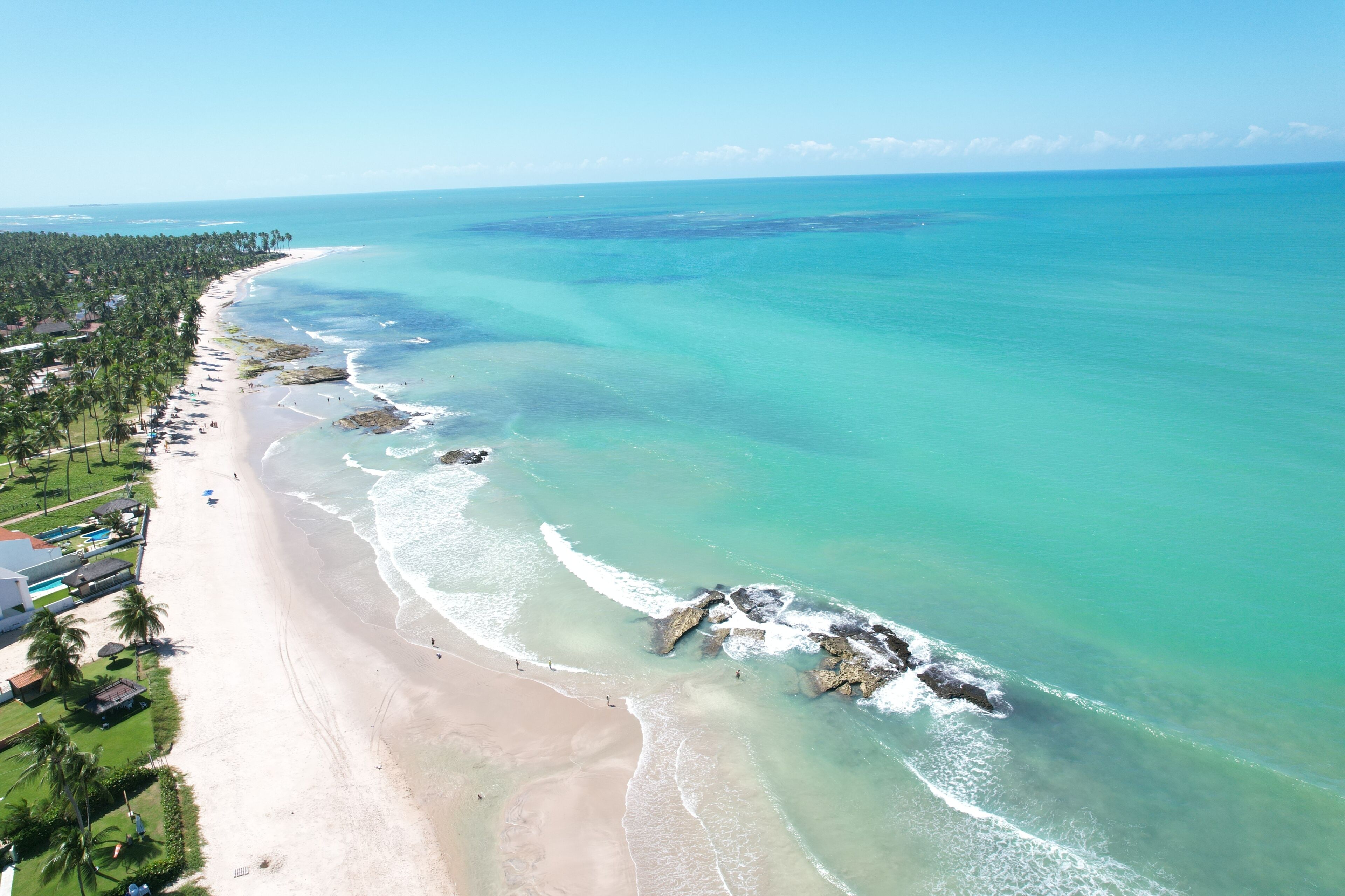 A coastal resort with a long sandy beach, clear turquoise waters, and a line of palm trees.