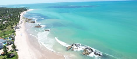 A coastal resort with a long sandy beach, clear turquoise waters, and a line of palm trees.