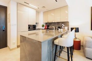 A modern kitchen with a central island, bar stools, and a seating area with a sofa. - Rentico l Luxury 1BR Burj Khalifa & Canal View (Dubai)