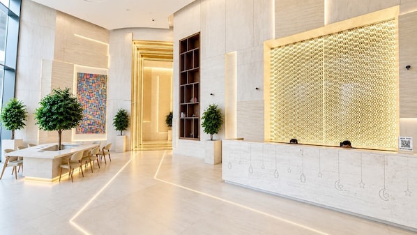 A modern hotel lobby with a reception desk, seating area, and a decorative wall. - Rentico l Luxury 1BR Burj Khalifa & Canal View (Dubai)