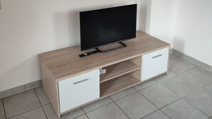 Una sala de estar moderna con un televisor de pantalla plana sobre un mueble de madera, un cuadro enmarcado arriba y piso de baldosas.