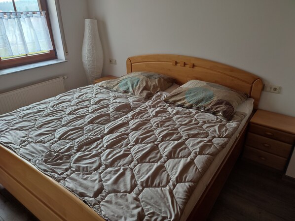 A neatly made bed with a quilted cover, a wooden headboard, and a bedside table with a drawer. - Quietly located vacation apartment (Altensteig)
