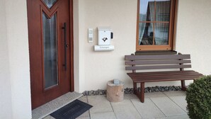 Una puerta de madera con un panel de vidrio, un banco, una jardinera de piedra y un portero automático en la pared.