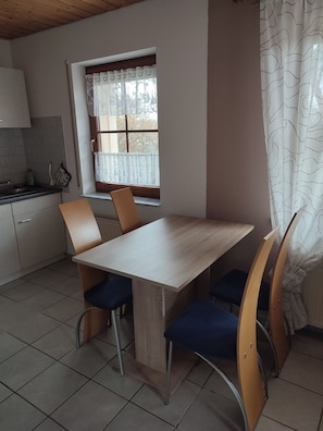 Eine kompakte Küche mit Essbereich, ausgestattet mit einem Holztisch und Stühlen, einem Fenster mit Spitzenvorhängen und einem gefliesten Boden.