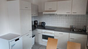 Una cocina compacta con armarios blancos, horno integrado, cafetera y lavamanos.