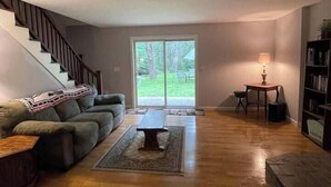 A spacious living room with a staircase, a sofa, a coffee table, and a bookshelf. - Acadia Coastal Cape 20 min to Acadia National Park (Lamoine)