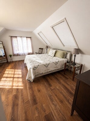 A bedroom with a bed, a chair, a lamp, a window with curtains, and a skylight.
